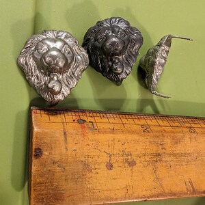 May include: Three silver lion head decorative metal pieces. The lion heads are detailed and have a textured finish.