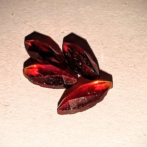 May include: Four deep red, faceted, teardrop-shaped crystals on a white background.