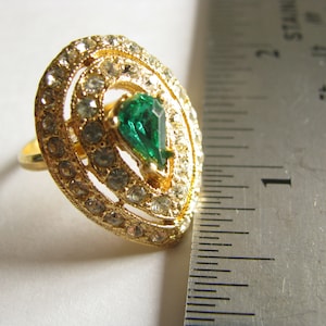 May include: A gold ring with a teardrop-shaped green stone surrounded by smaller clear stones.