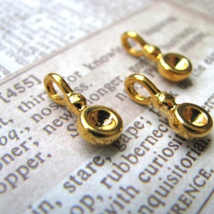 May include: Three gold-toned metal charms with a loop at the top and a round, slightly concave disc at the bottom. The charms are on a white surface with printed text.