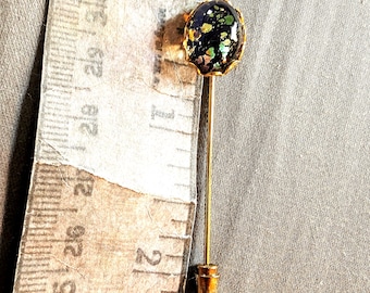 May include: A gold tie tack with a black and green iridescent glass cabochon. The cabochon has a gold rim.