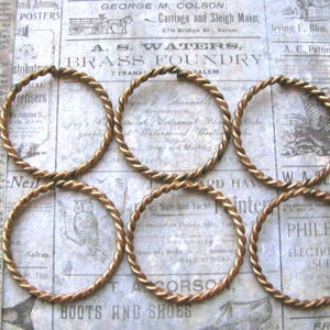 May include: Six gold-colored twisted wire rings. The rings are all the same size and are arranged in a semi-circle on a vintage newspaper background.