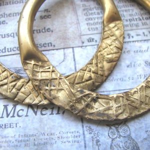 May include: Two gold-toned hoop earrings with a textured, criss-cross pattern. The earrings are thick and substantial.
