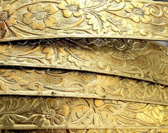 May include: Close-up of four gold-colored metal strips with an intricate floral design embossed into the surface.