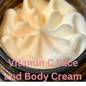 Könnte beinhalten: Nahaufnahme eines Creme-Glases mit einem Wirbel aus weißer und pfirsichfarbener Creme. Das Glas hat einen schwarzen Deckel und der Text "Vitamin C Face and Body Cream" ist auf der Vorderseite aufgedruckt.
