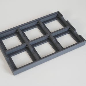May include: A rectangular, dark gray plastic tray with six square compartments. The tray has a raised border and is designed to hold small items. The interior of each compartment is white.