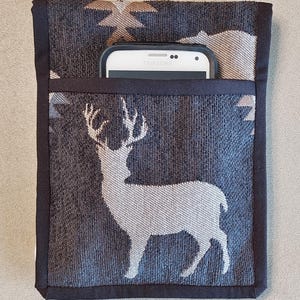 Könnte beinhalten: Eine dunkelgraue Handytasche mit einer weißen Hirschsilhouette und Sternenmuster. Die Tasche hat einen schwarzen Rand und eine Tasche mit einem weiß-schwarzen Samsung-Handy. Die Handyhülle ist sichtbar.