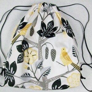 May include: A white drawstring bag with black and gray floral and bird designs. The bag has black drawstrings.