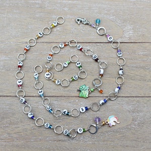 May include: A silver chain necklace with white beads numbered 0-9. The necklace has colorful beads and charms, including a leaf and a unicorn.