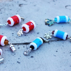 May include: Six colorful, small, round, glass bead counter charms with silver metal charms attached. The beads are red, blue, and white. The charms include a snowflake, a mitten, a paw print, a house, a hat, and a hand.