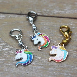 May include: Three silver and gold unicorn stitch markers with rainbow manes. The unicorn heads are white with rainbow colored manes and a single horn.