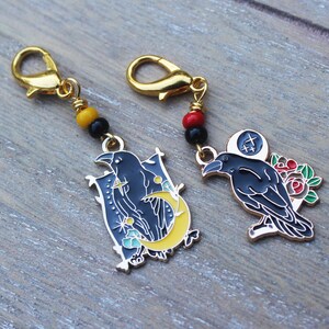 May include: Two black crow charms with gold accents and colorful beads. One charm features a crow with a crescent moon and stars. The other charm features a crow with red roses.