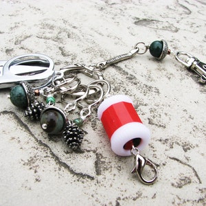 May include: A silver key chain with a variety of charms, including a small pair of scissors, a red and white spool, and several green and brown acorn-shaped charms.