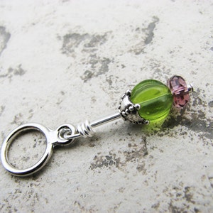 May include: A silver charm with a green glass bead and a pink glass bead. The charm has a ring at the top for attaching to a bracelet or necklace.
