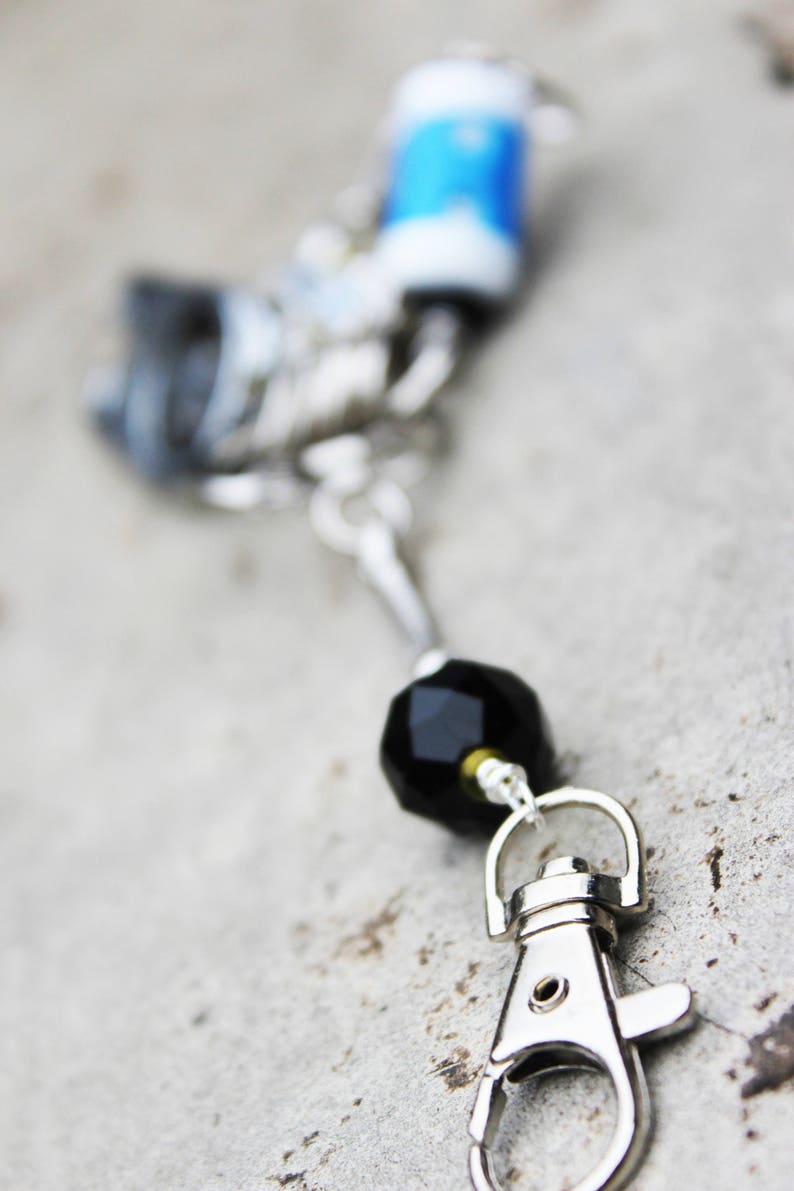 Peut inclure: Un porte-cl&eacute;s argent&eacute; avec une perle noire et un fermoir argent&eacute;. Le porte-cl&eacute;s a un charme bleu et blanc attach&eacute; &agrave; lui.