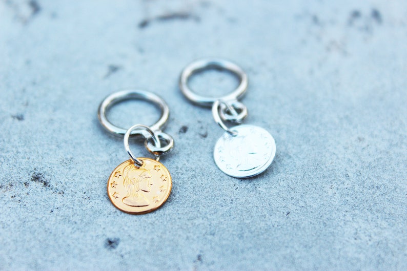 Peut inclure: Deux porte-cl&eacute;s argent&eacute;s avec des breloques rondes en m&eacute;tal. Un charme est en or et pr&eacute;sente un profil de femme. L'autre charme est en argent et pr&eacute;sente un motif.