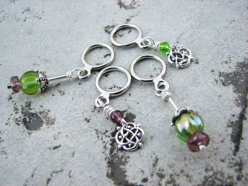 May include: Four silver stitch markers with green and purple glass beads and silver Celtic knot charms.