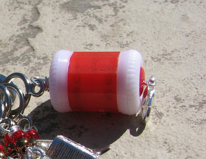 Peut inclure: Un porte-cl&eacute;s rouge et blanc avec un anneau argent&eacute;. Le charme est en forme de petit cylindre avec un dessus blanc et un fond rouge.