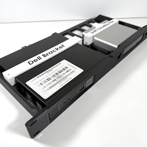 Peut inclure: Un support Dell noir avec une étiquette blanche indiquant "Dell Bracket". Un UniFi Cloud Key Plus argenté est également visible sur l'image.