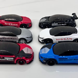 May include: Six toy cars, all Nissan models, in different colors: red, silver, white, black, and blue. Each car has the words "Nissan Intelligent Mobility" printed on the side.