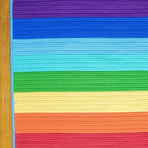 May include: A rainbow-colored crocheted rug with stripes of purple, blue, turquoise, green, yellow, orange, and red.