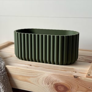 Op de afbeelding: Een ovale, donkergroene plantenbak met een geribbeld ontwerp. De plantenbak is gemaakt van een glad, mat materiaal.