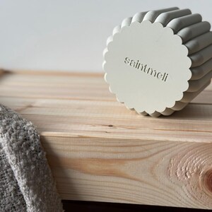 May include: A white ceramic planter with a scalloped edge and the text "saintmeli" embossed on the bottom. The planter is sitting on a light wood surface.