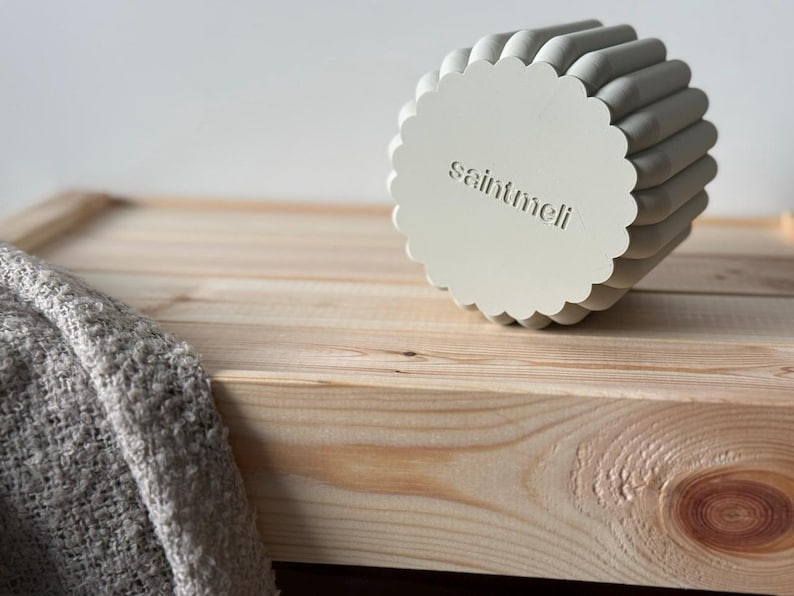 May include: A white ceramic planter with a scalloped edge and the text "saintmeli" embossed on the bottom. The planter is sitting on a light wood surface.