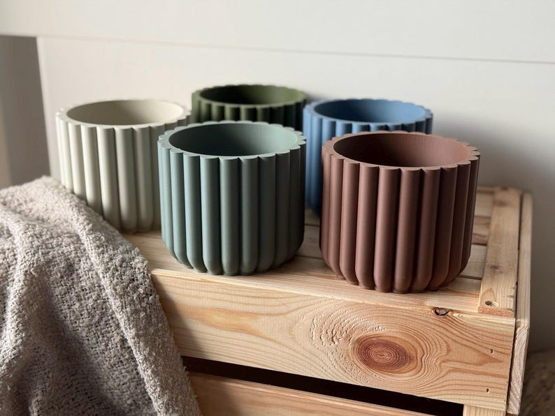 May include: Five different colored concrete planters with a ribbed design. The planters are arranged on a wooden shelf.
