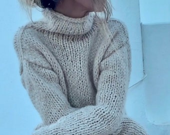 Könnte beinhalten: Eine Frau trägt einen hellbraunen Strickpullover mit Rollkragen und einen weißen Rock. Sie trägt braune Wildlederstiefel, die bis zum Knie reichen.