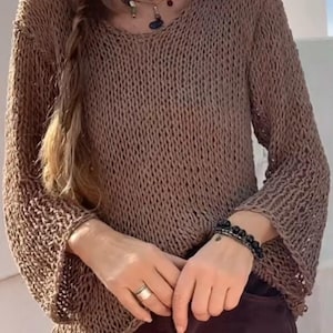 Könnte beinhalten: Ein brauner Strickpullover mit lockerer Passform und langen Ärmeln. Der Pullover hat einen V-Ausschnitt und ein zartes Lochmuster.