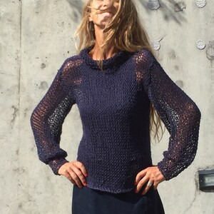May include: A navy blue knitted jumper with a loose fit and long sleeves. The jumper has a delicate openwork pattern throughout.