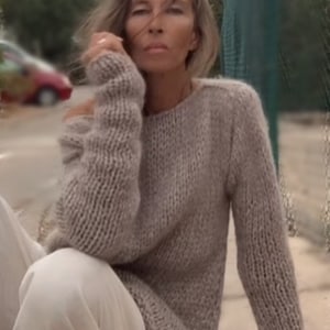 Op de afbeelding: Een vrouw draagt een loszittende, lichtbruine gebreide trui met een licht oversized pasvorm. De trui heeft een ontspannen, casual stijl en is gemaakt van een zacht, getextureerd garen.
