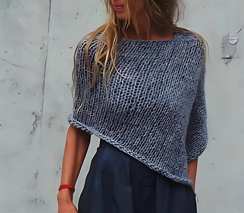 May include: A grey knitted sweater with a loose, boxy fit and short sleeves. The sweater has a slightly asymmetrical hemline.