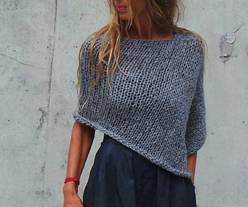 May include: A grey knitted sweater with a loose, oversized fit and a slightly asymmetrical hem.