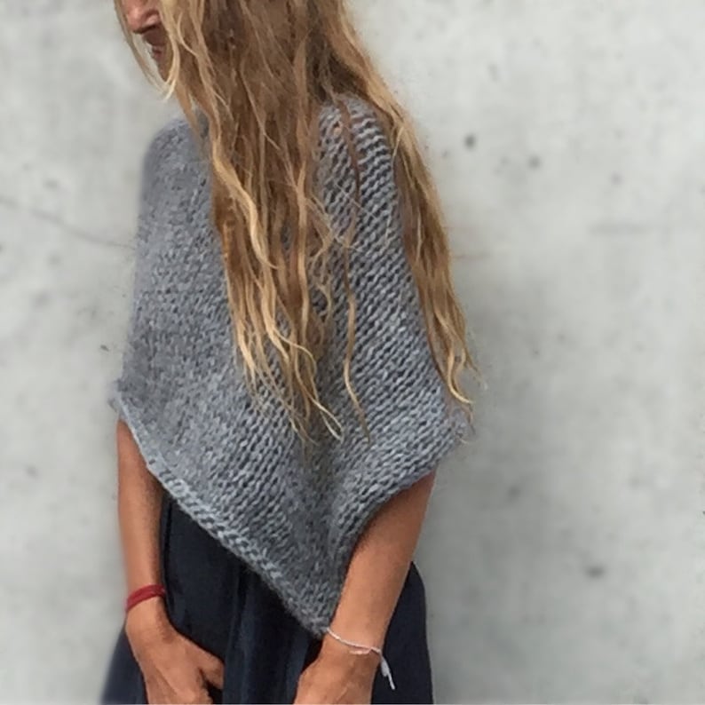 May include: A grey knitted poncho with a loose, flowing fit. The poncho is made from a soft, lightweight yarn and has a simple, elegant design.