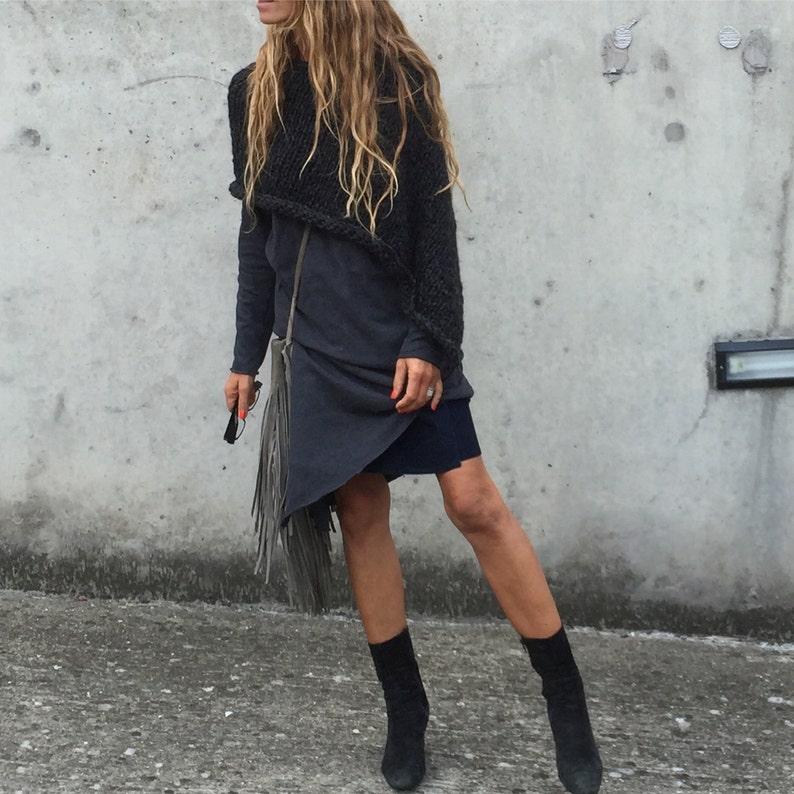 May include: A woman wearing a black knit sweater and a long, dark grey dress with a fringe bag. She is wearing black ankle boots.