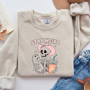 Stay Weird グラフィック T シャツ - 風変わりなスケルトンとポッサムのデザイン、かわいいコーヒー T シャツ、楽しくてユニークなギフトのアイデア、ハロウィーンのスウェットシャツとシャツ"