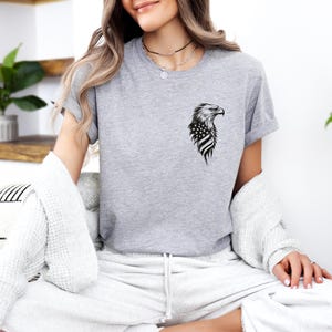 May include: A gray t-shirt with a black and white graphic of an eagle with an American flag on its chest.
