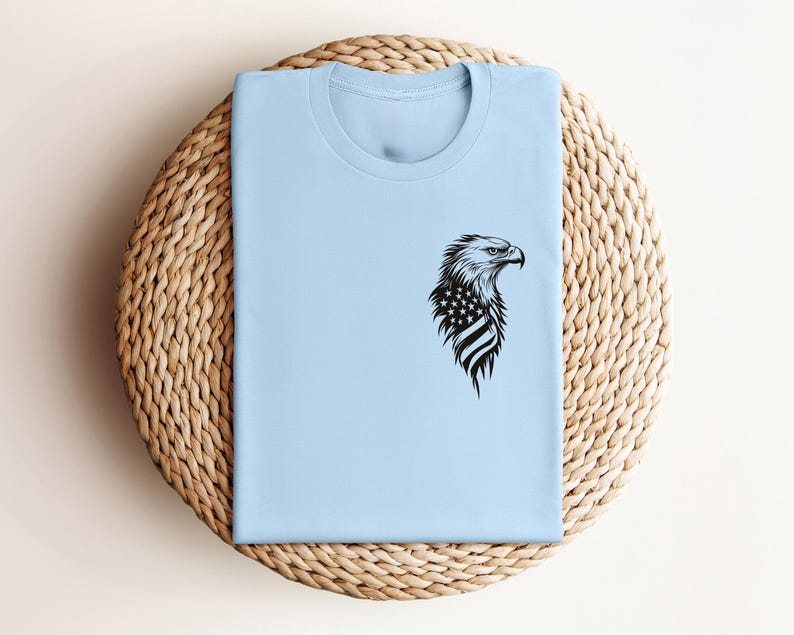 May include: A light blue t-shirt with a black and white graphic of an eagle's head with an American flag on its chest.