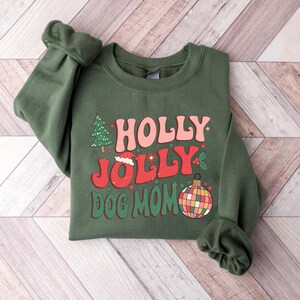 May include: Green Christmas sweatshirt with the text "HOLLY JOLLY DOG MOM" in a retro font. The design includes a Christmas tree, a Santa hat, and a colorful ornament.