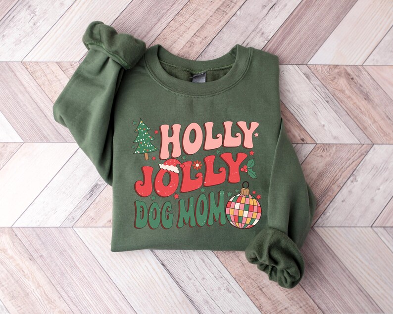 May include: Green Christmas sweatshirt with the text "HOLLY JOLLY DOG MOM" in a retro font. The design includes a Christmas tree, a Santa hat, and a colorful ornament.