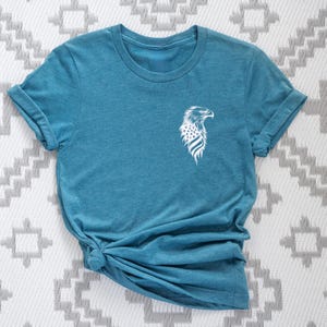 May include: A teal blue t-shirt with a white graphic of an eagle with an American flag design.