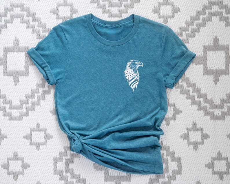 May include: A teal blue t-shirt with a white graphic of an eagle with an American flag design.