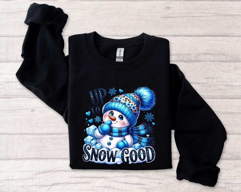 Peut inclure: Sweat-shirt noir avec un motif de bonhomme de neige bleu et blanc. Le bonhomme de neige porte un chapeau et une &eacute;charpe bleus et est entour&eacute; de flocons de neige bleus. Le texte "Up to Snow Good" est imprim&eacute; sous le bonhomme de neige.