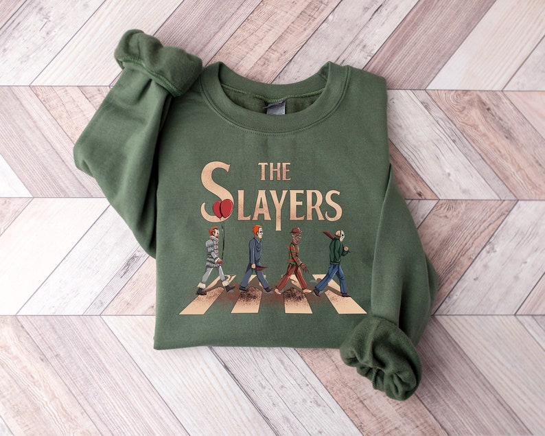 May include: A green sweatshirt with a graphic of horror movie characters walking across a crosswalk. The graphic says "The Slayers" with a red balloon.