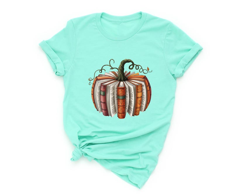 May include: A mint green short-sleeve t-shirt featuring a central graphic of a pumpkin constructed from open books. The pumpkin has a dark green stem with curling vines and pages fanned out to form the round shape of the gourd.