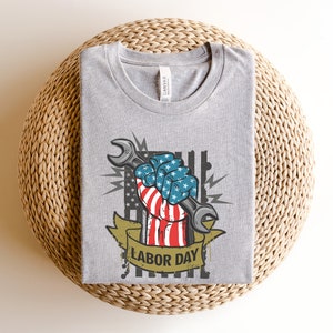 May include: Gray t-shirt with a graphic of a fist holding a wrench. The fist is wrapped in an American flag and the text "Labor Day" is below the graphic.