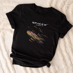 May include: Black t-shirt with a white SpaceX logo and the text "Flight 7" with a graphic of a rocket launch trail.