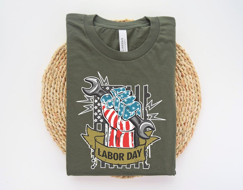 May include: A green t-shirt with a graphic of a hand holding a wrench. The hand is painted with the American flag and the text "Labor Day" is below the graphic.